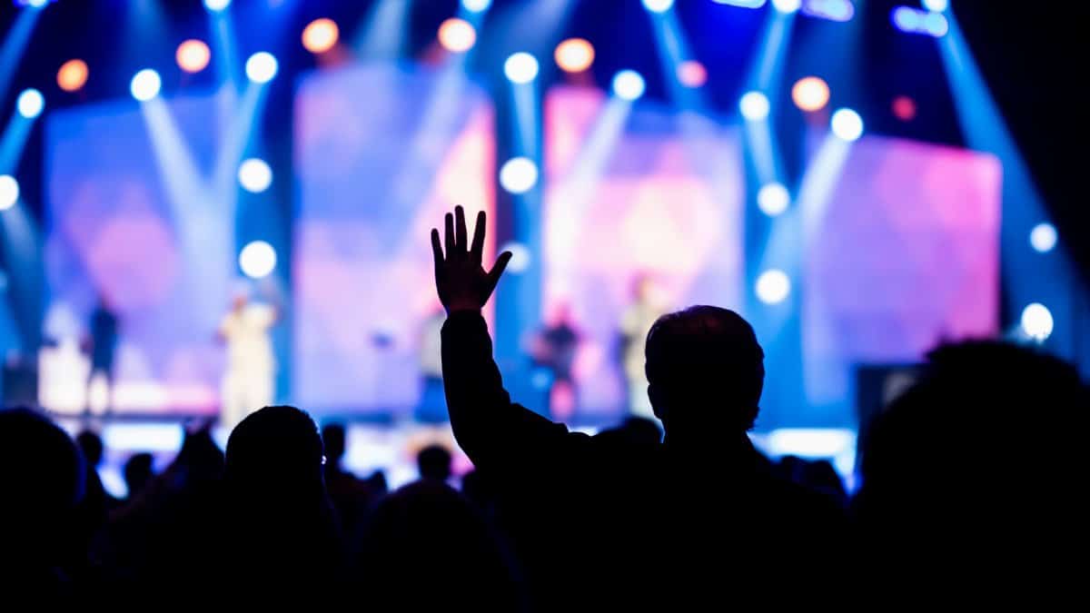 Silhouette of an audience member reaching out towards a brightly lit concert stage.