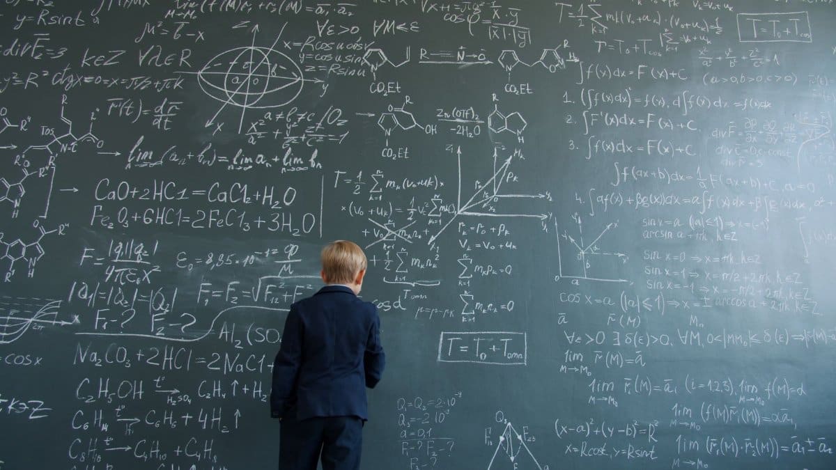 Child in suit solving complex mathematical equations on a chalkboard.