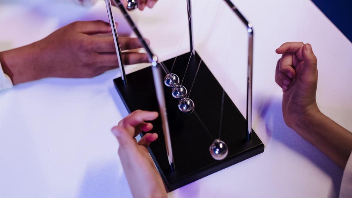 Close-up of hands interacting with a Newton's cradle on a white table in a studio setting.