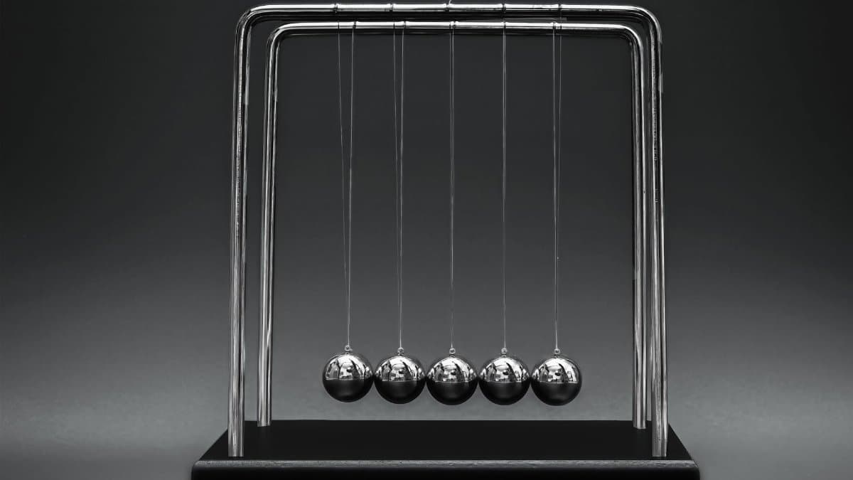 Close-up image of Newton's Cradle illustrating physics concepts on a dark gray background.