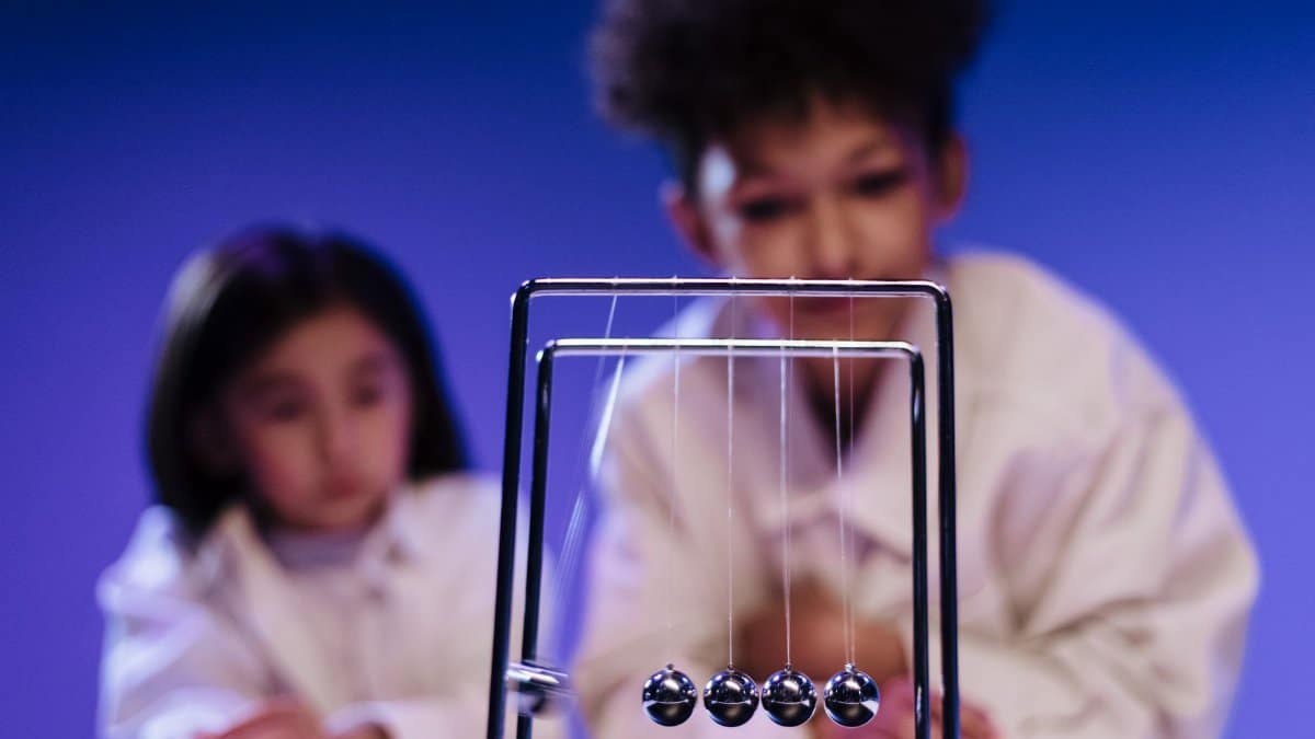 Two children curiously observing a Newton's Cradle in a science setting.