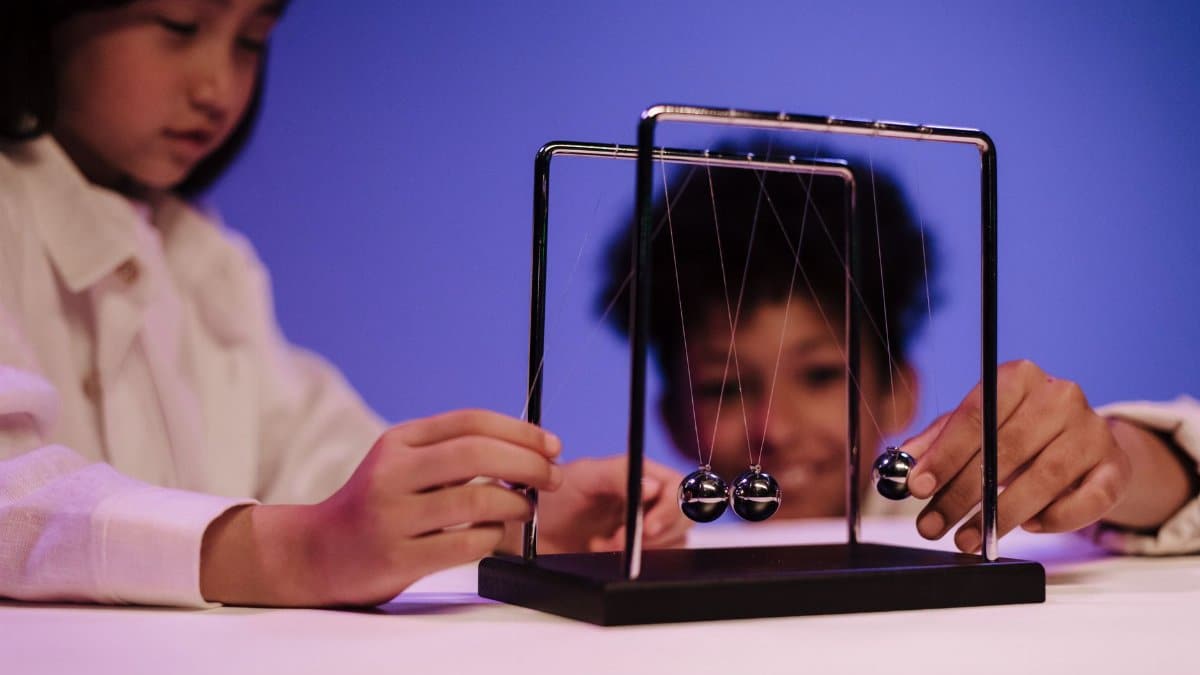 Two diverse children exploring physics concepts with a Newton's Cradle in a studio.