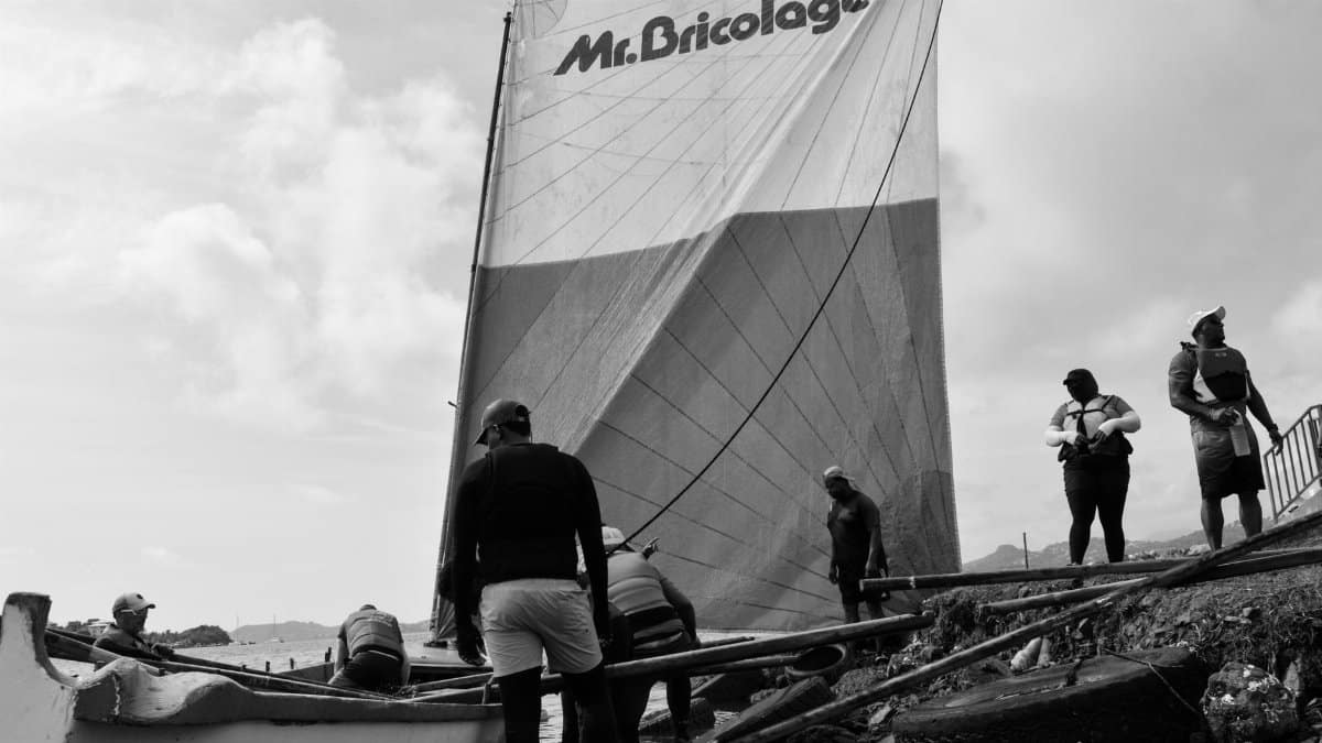 Sailing team collaborating to launch a boat with Mr. Bricolage branded sail.