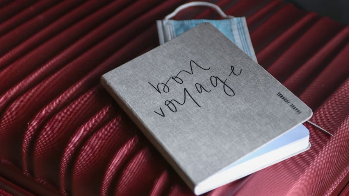 Close-up of a travel journal and mask on a red suitcase, symbolizing preparation for a voyage.