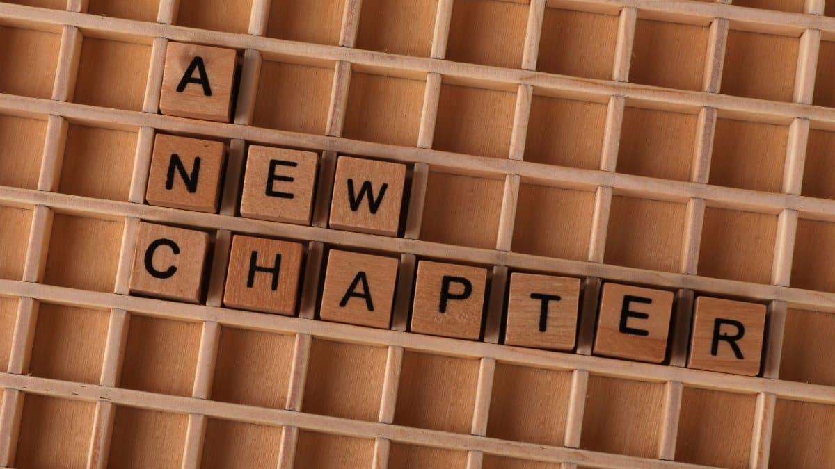 Scrabble tiles spelling 'A New Chapter' on wooden grid, symbolizing new beginnings.