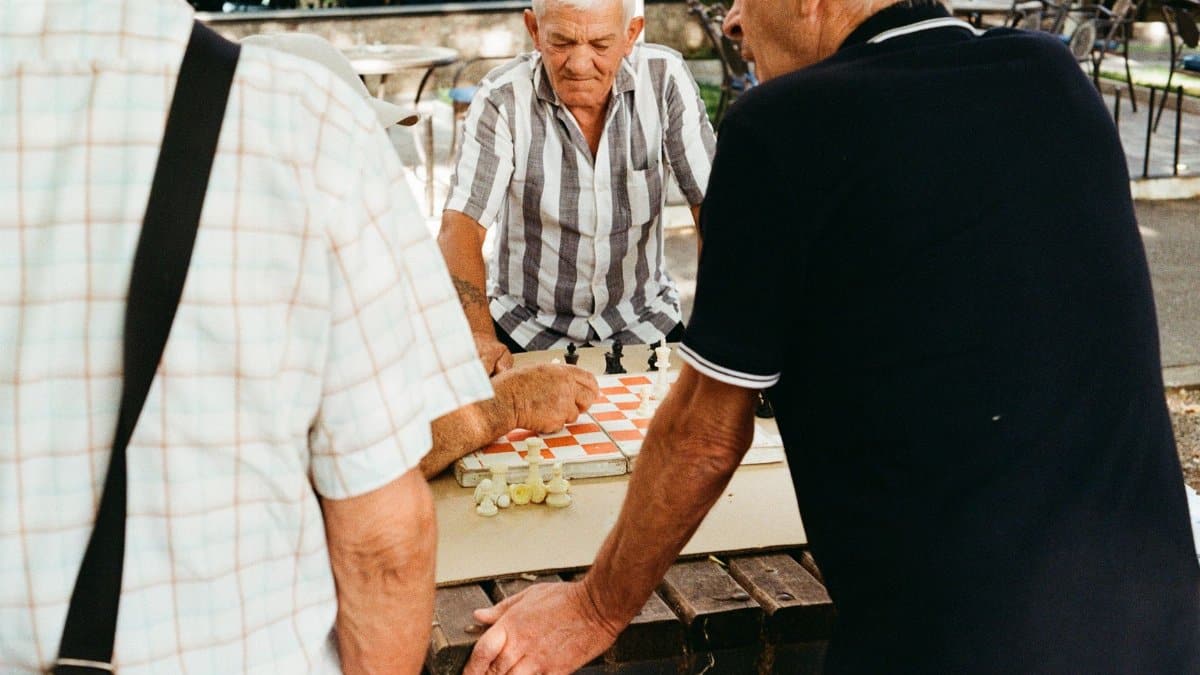 Three senior men playing a chess game outdoors, enjoying a sunny day.