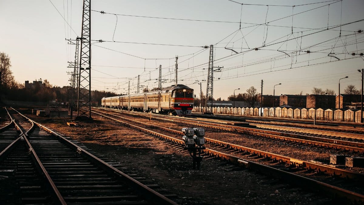 A train travels on railway tracks surrounded by infrastructure and power lines during sunset.