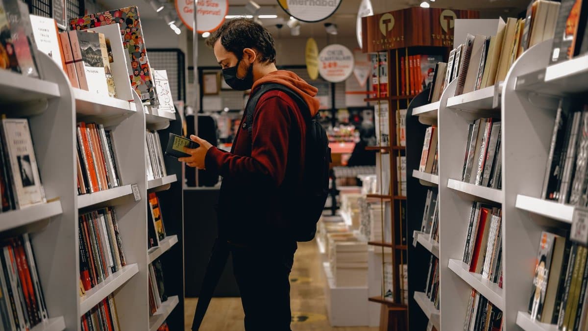Person wearing mask browsing a bookshelf in a modern bookstore during pandemic.