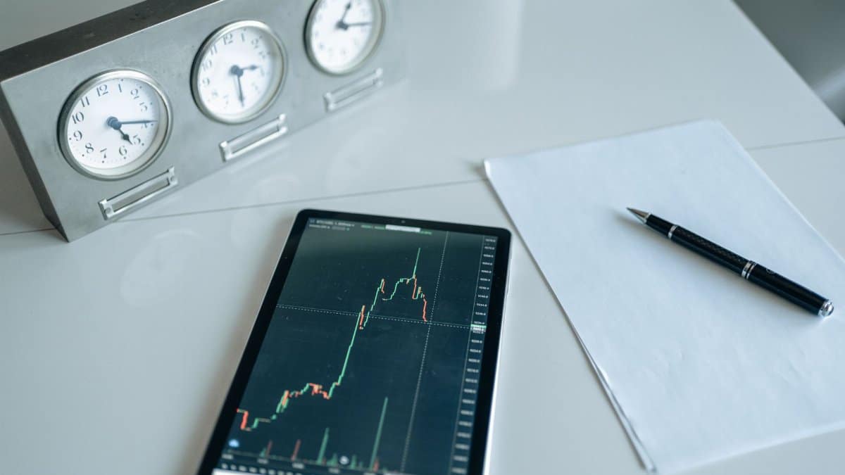 A desk with trading tools, including a tablet showing stock market data and three clocks.