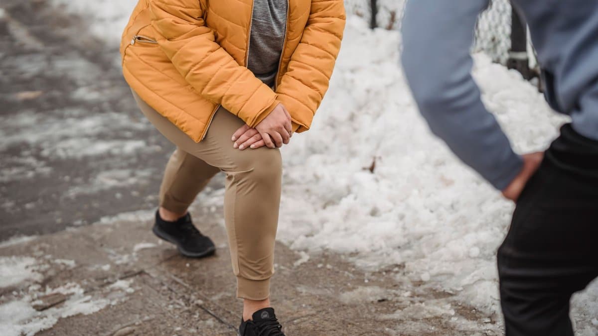 Unrecognizable plump woman in warm outerwear doing stretching exercise with anonymous personal trainer while training in winter park with snow