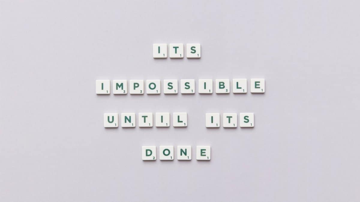 Motivational phrase 'It's impossible until it's done' arranged with Scrabble tiles on a gray background.