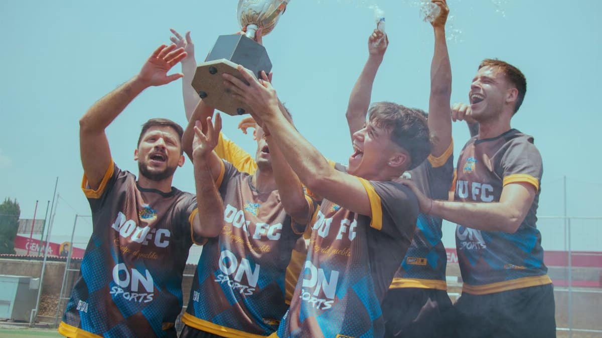 A jubilant soccer team celebrates their championship victory by raising a trophy outdoors.