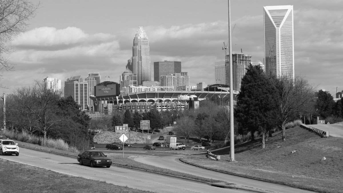 A black and white photograph of Charlotte's skyline featuring roads and moving vehicles.