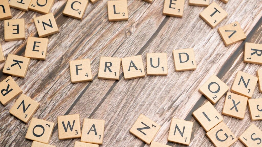 Alphabet tiles arranged to spell 'fraud' on a wooden surface, symbolizing deception.