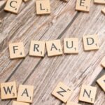 Alphabet tiles arranged to spell 'fraud' on a wooden surface, symbolizing deception.