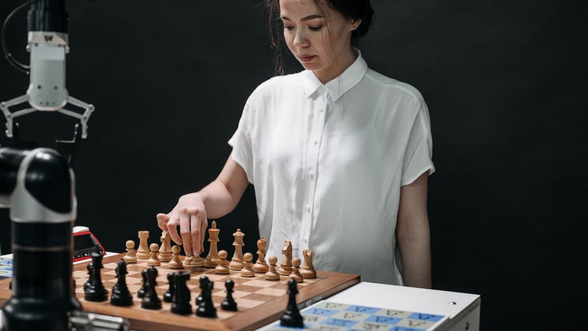 A woman plays chess with a robotic arm, illustrating technology and strategy in a modern context.