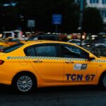 A vibrant yellow taxi speeds along a bustling city street during nighttime.