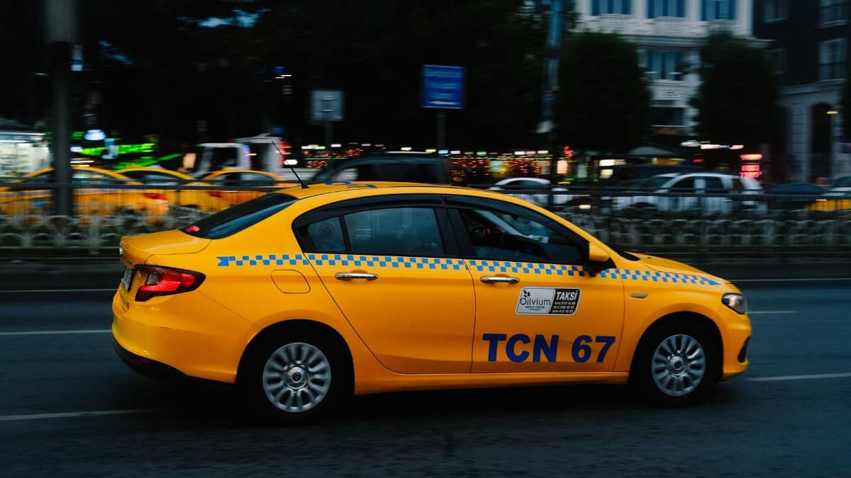 A vibrant yellow taxi speeds along a bustling city street during nighttime.