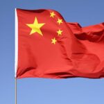 Chinese national flag flying high against a clear blue sky, symbolizing unity and pride.