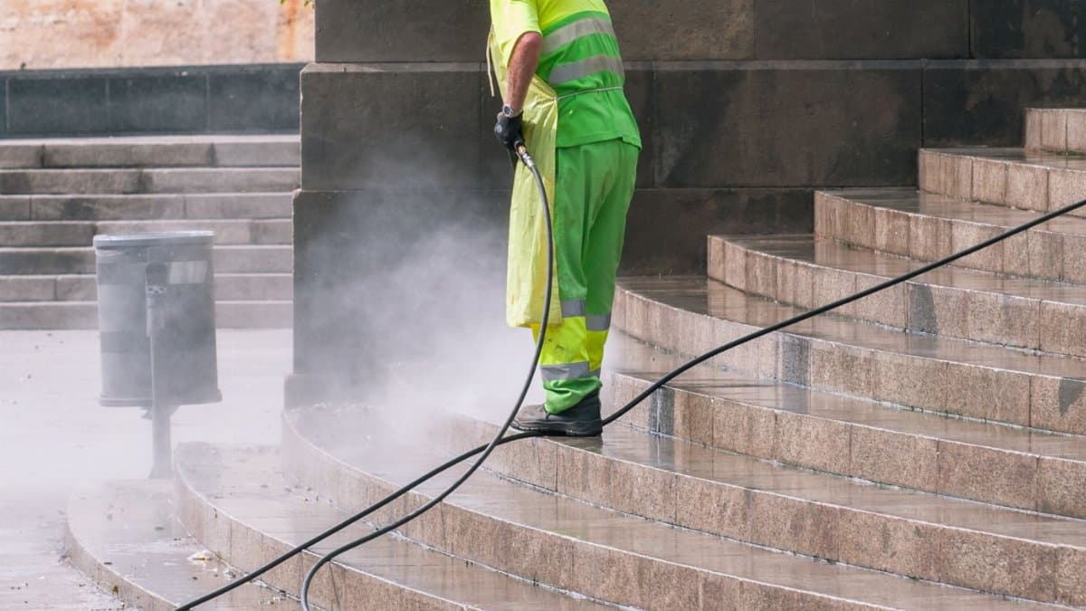 A street worker pressure washes stone stairs in a public park, ensuring cleanliness and safety.