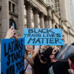 A vibrant city protest advocating for Black Trans rights with diverse participants holding signs.