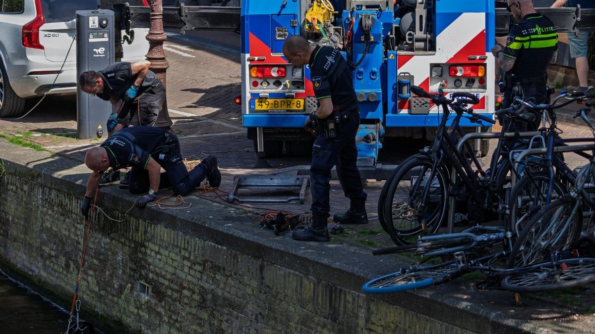 Police officers conducting a canal search operation in a city with bicycles nearby.