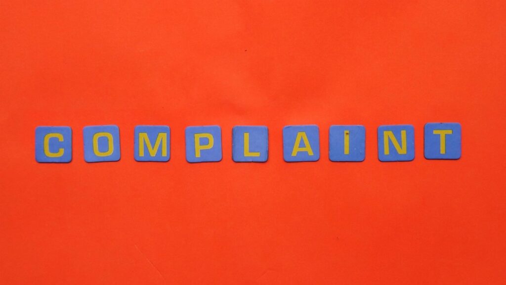 Blue letter tiles spelling 'COMPLAINT' on a vibrant red surface.