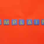 Blue letter tiles spelling 'COMPLAINT' on a vibrant red surface.