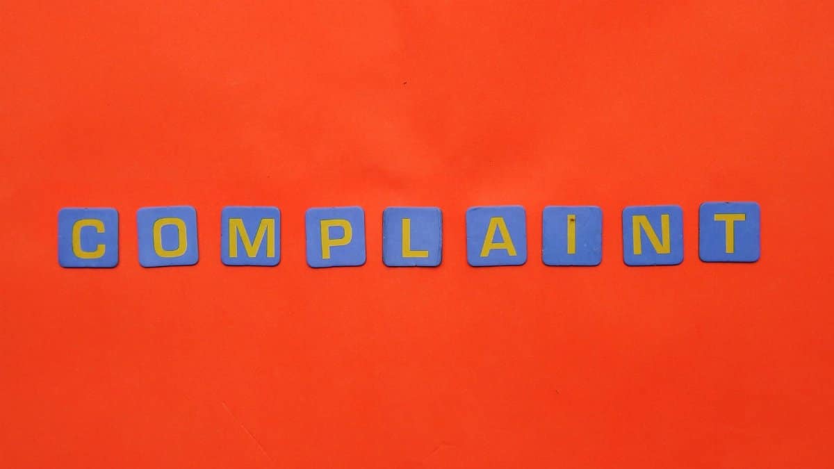 Blue letter tiles spelling 'COMPLAINT' on a vibrant red surface.