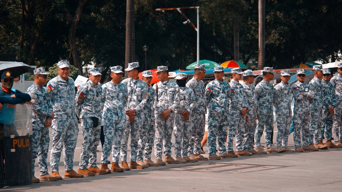 A group of soldiers in camouflage uniforms standing in line outdoors during the day.