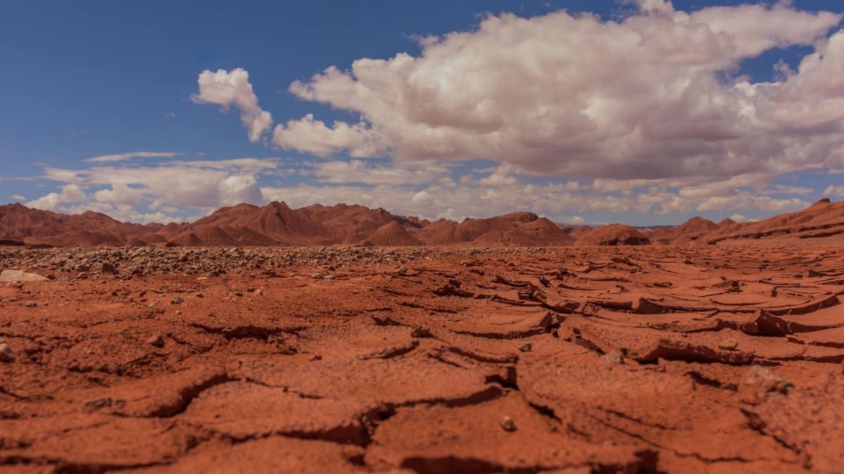 A stunning view of a cracked red desert under a bright blue sky with scattered clouds.