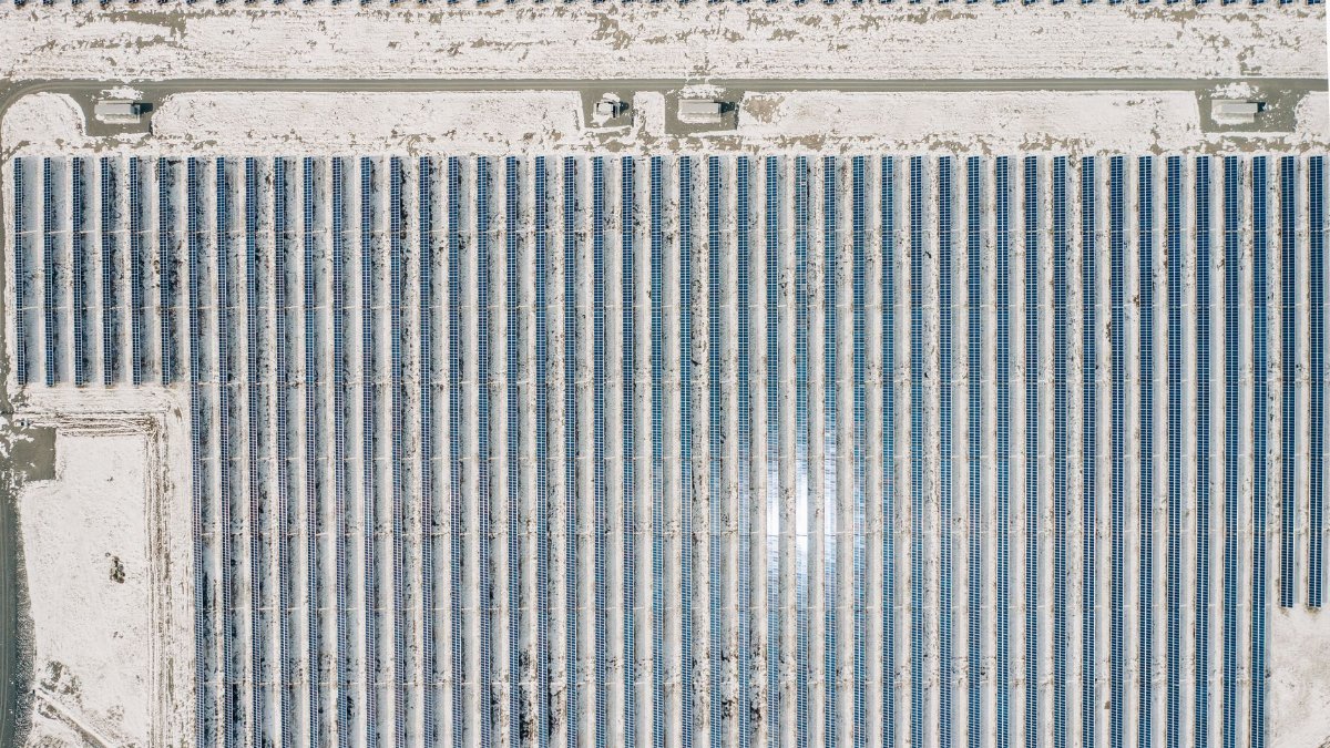 Drone shot of a solar farm amidst snow-covered terrain, showcasing renewable energy.