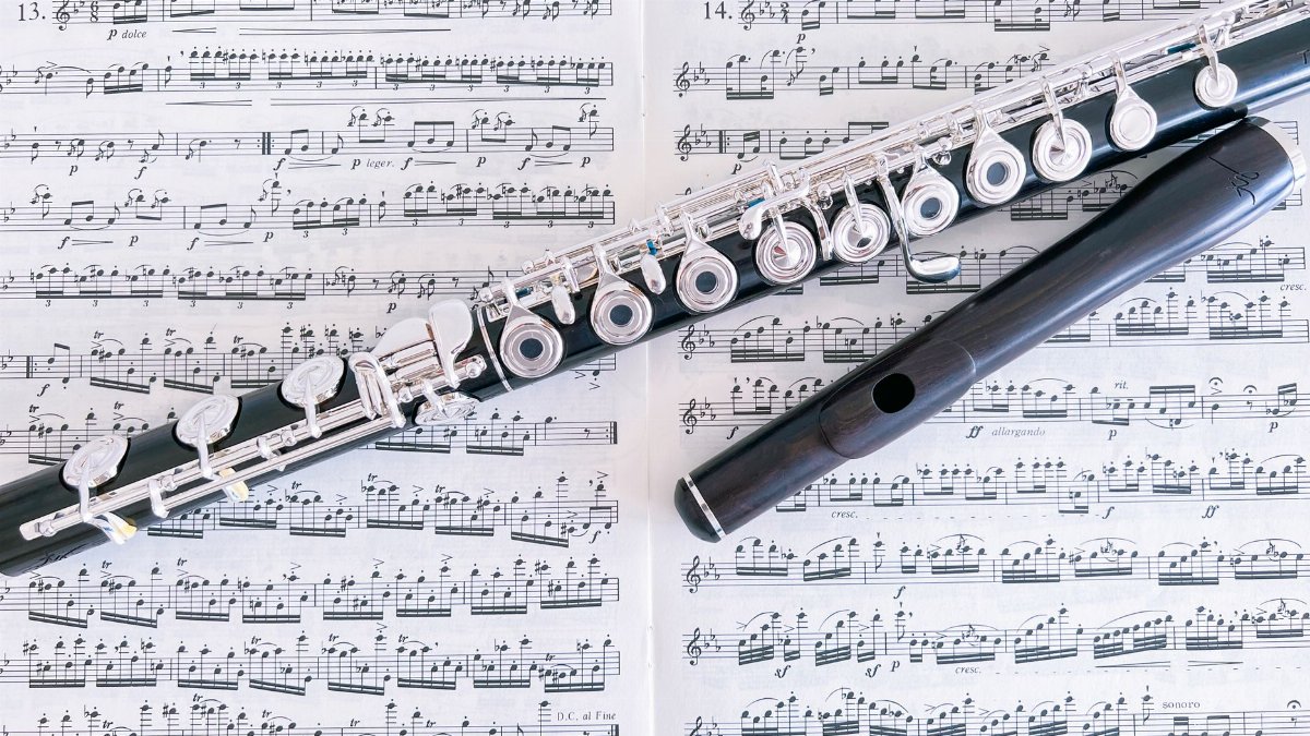 Close-up of a flute resting on sheet music pages, emphasizing musical composition.