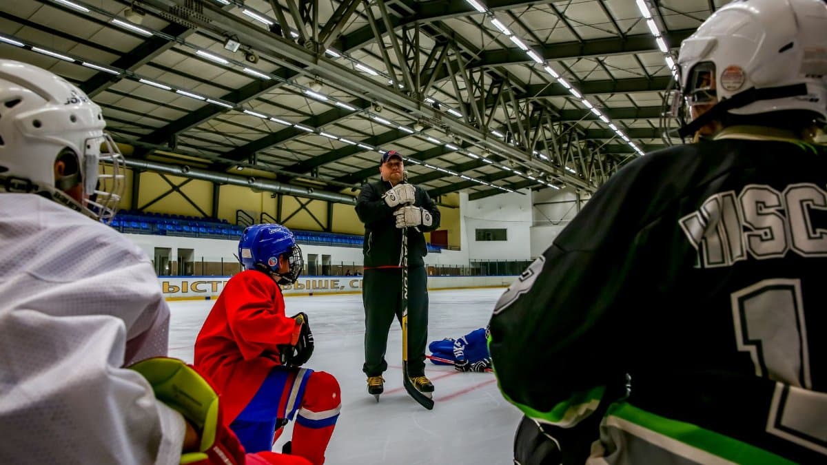 Ice hockey players and coach during a training session in an indoor ice arena.