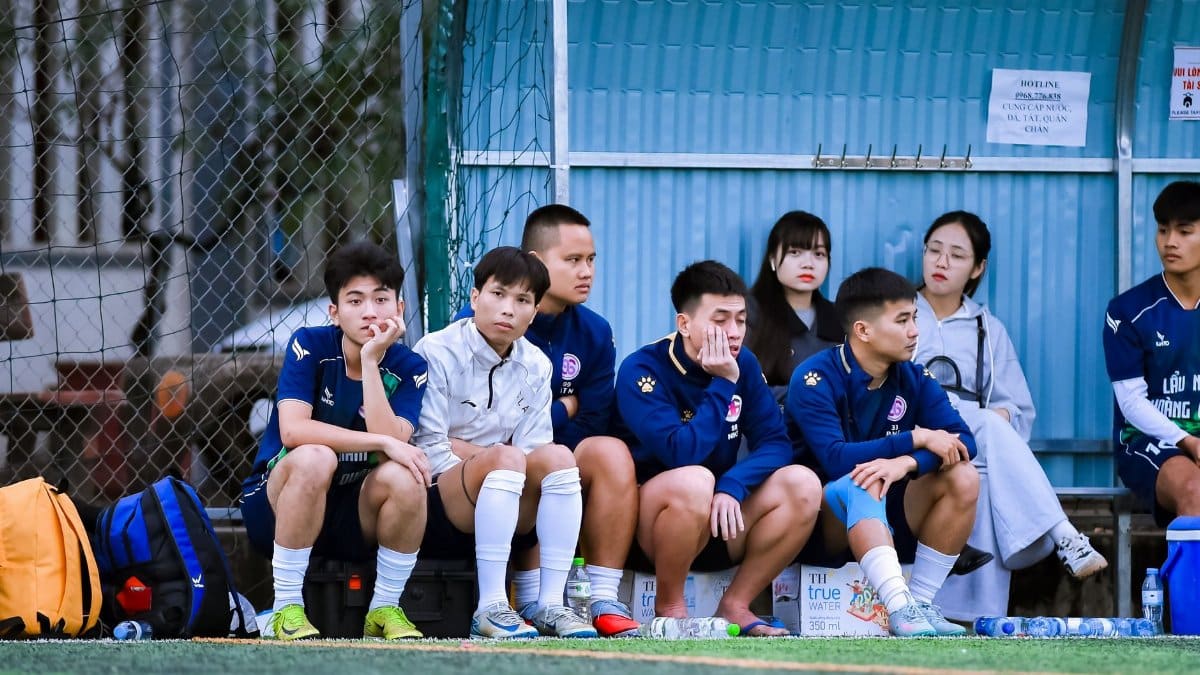 Football players and spectators on a bench during a match in Hanoi, Vietnam.