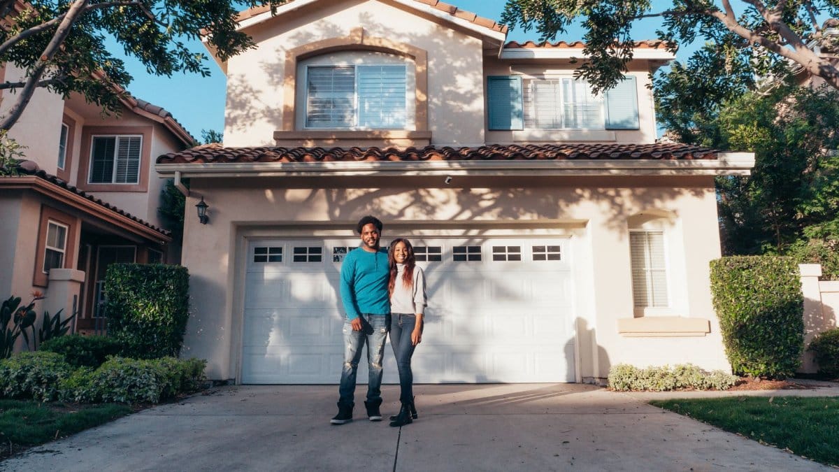 Smiling couple standing outside their newly purchased house on a sunny day.