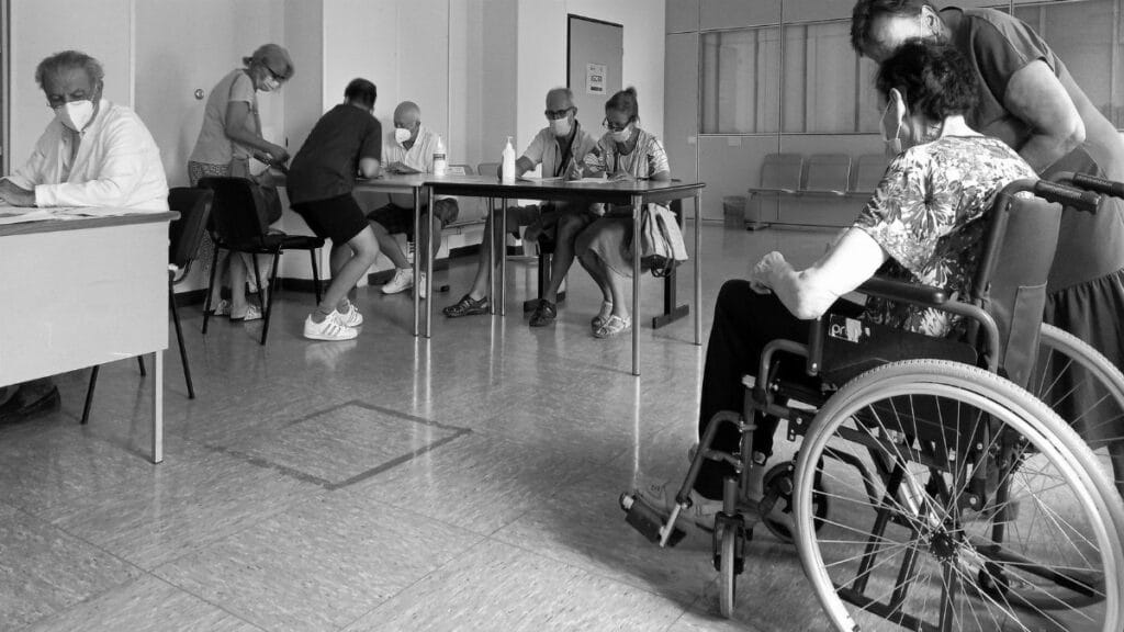 People wearing masks in a hospital waiting room, interacting and maintaining social distance.