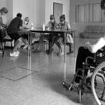 People wearing masks in a hospital waiting room, interacting and maintaining social distance.