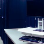 Contemporary computer with black screen placed on stand near row of server steel racks in data center