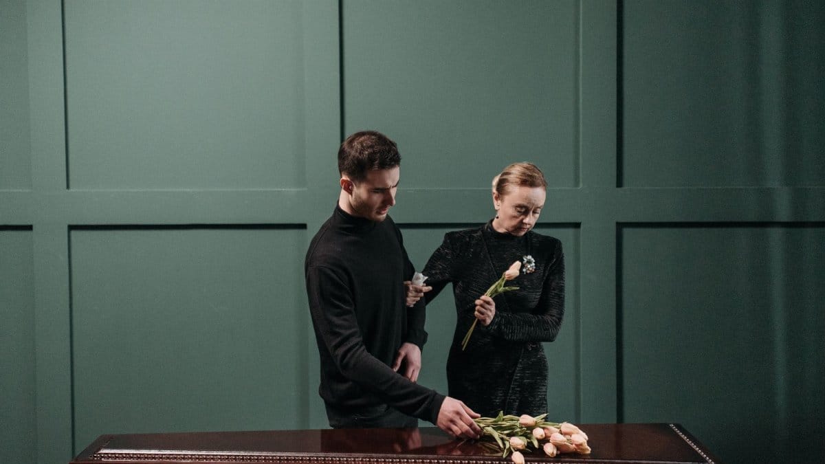 A somber moment of two relatives paying respects at a funeral indoors.