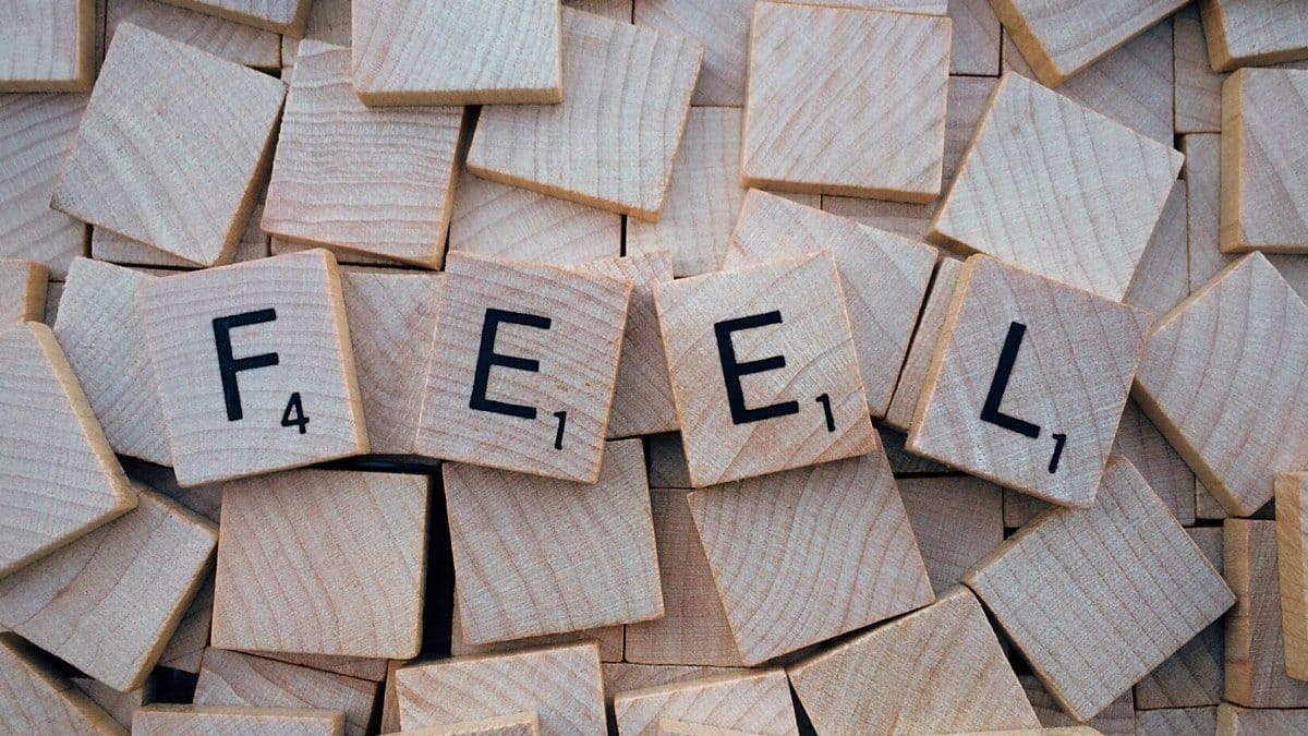 Close-up of Scrabble tiles spelling 'Feel' scattered on a wooden background.