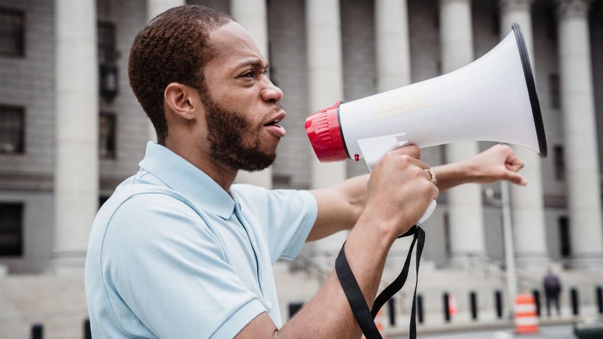 A young man passionately addresses a crowd during a protest with a megaphone.