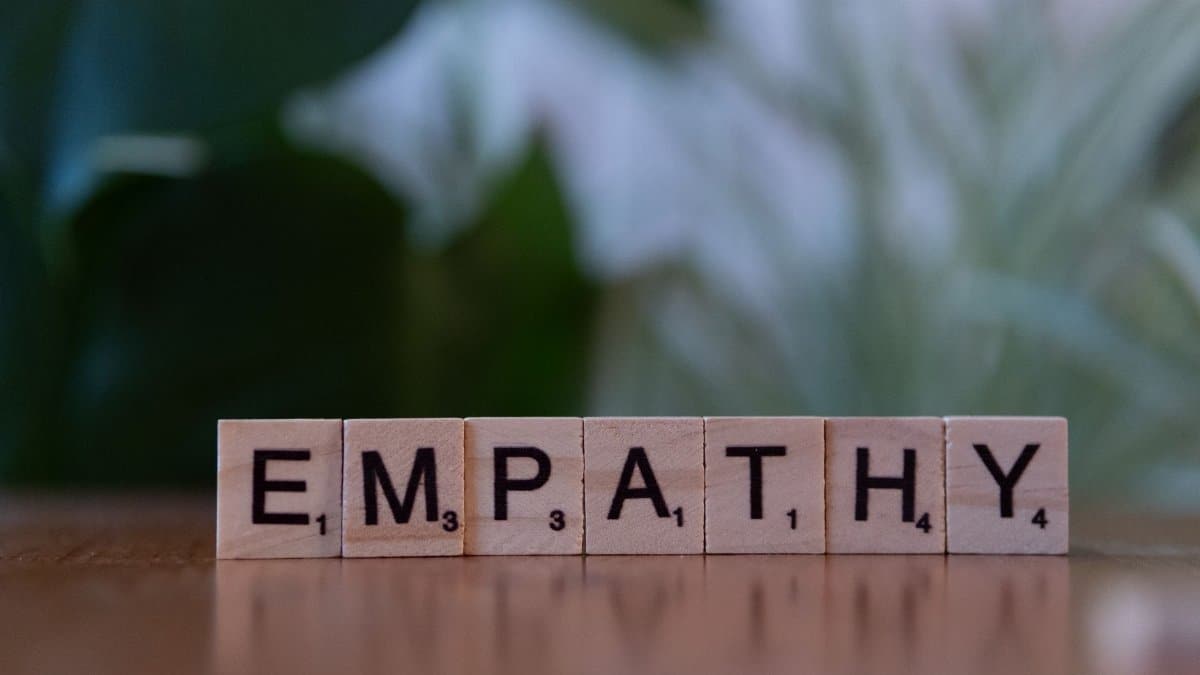Close-up of tiles spelling empathy on a wooden surface with blurred green background.