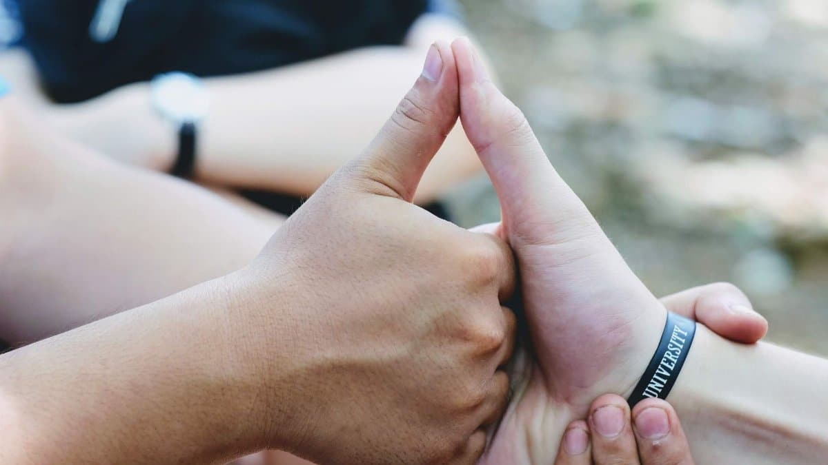 Close-up of hands forming a unity symbol, featuring diverse skin tones and a 'university' bracelet.