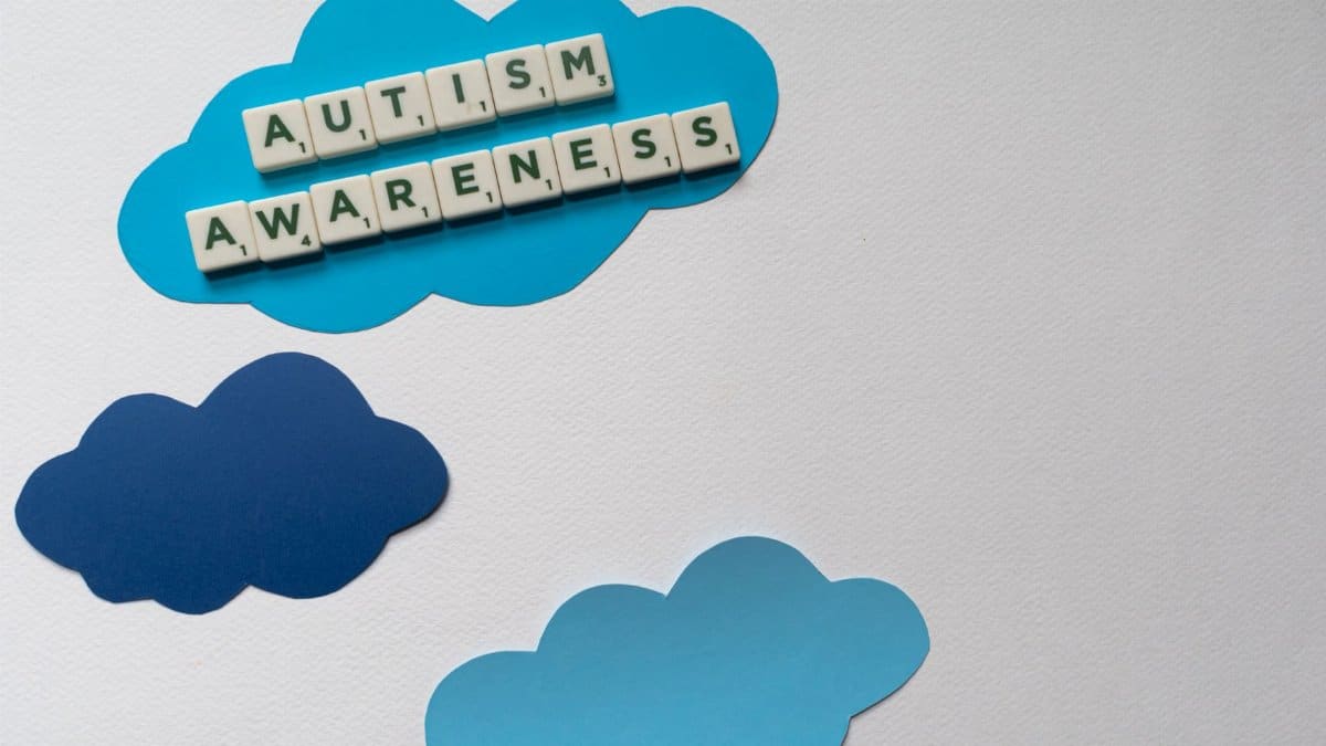 Flat lay of scrabble tiles spelling 'Autism Awareness' on blue cloud cutouts, ideal for awareness campaigns.