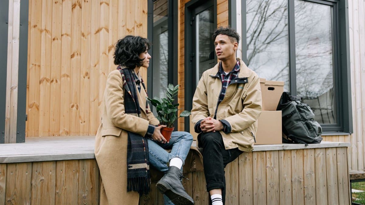 A young couple sitting on a porch with moving boxes, signifying moving in or starting anew.