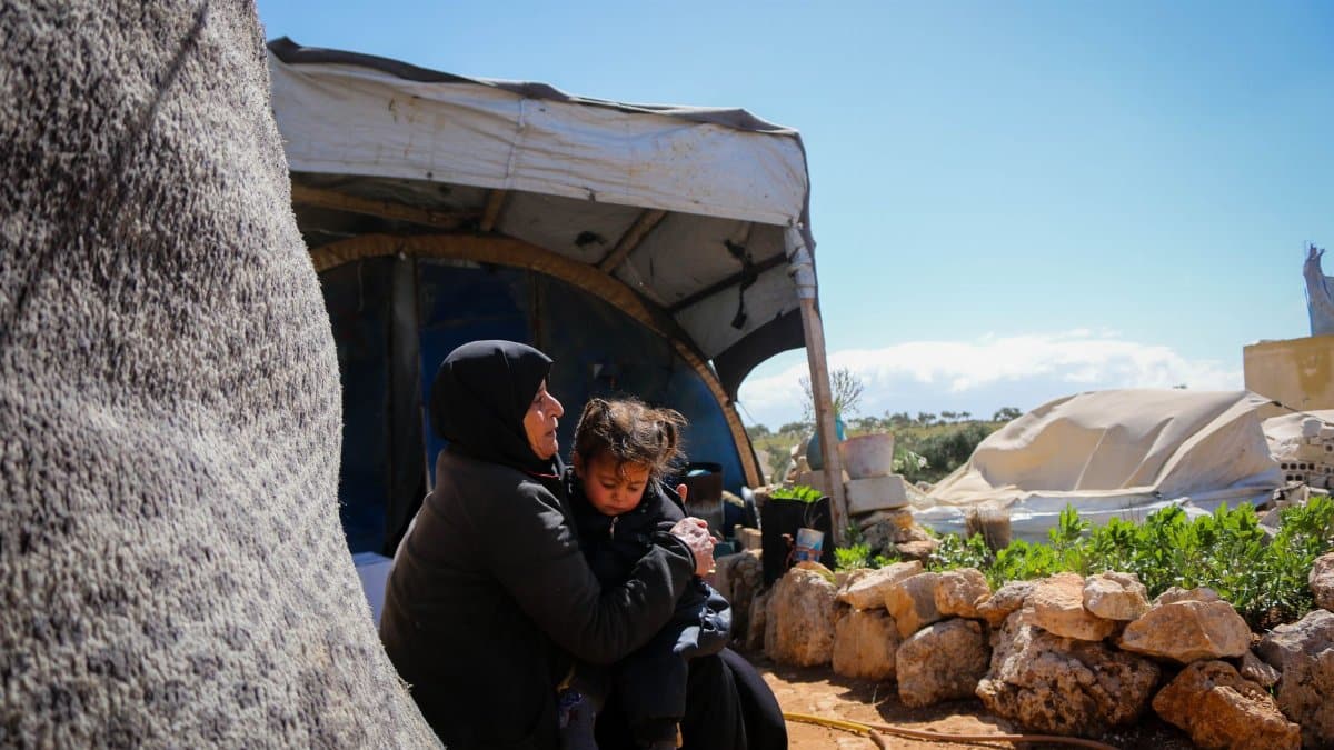 A mother comforts her child in a Syrian refugee camp, highlighting resilience and family bonds.