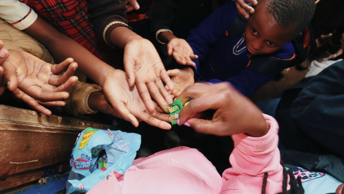 A group of children reaching out for candy being distributed in a community environment.