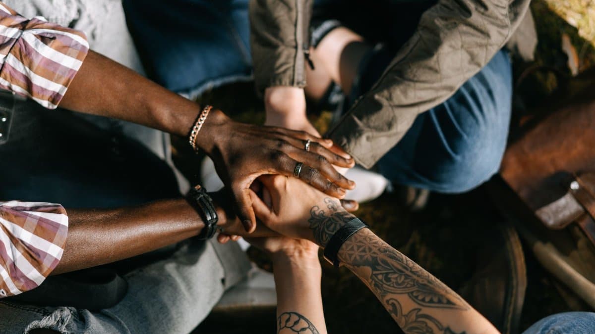 A diverse group of individuals uniting in solidarity with hands stacked together outdoors.