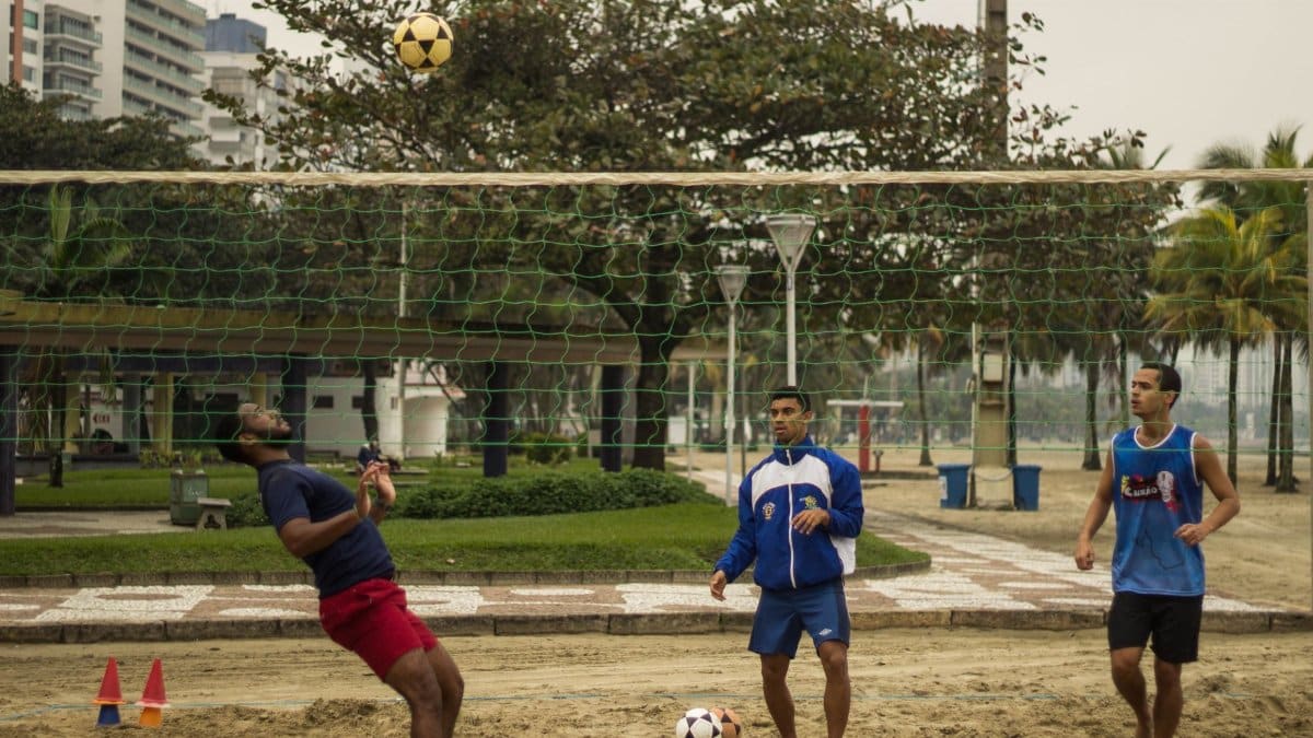 Three men engaging in a casual soccer game in an urban park environment, featuring net and ball.